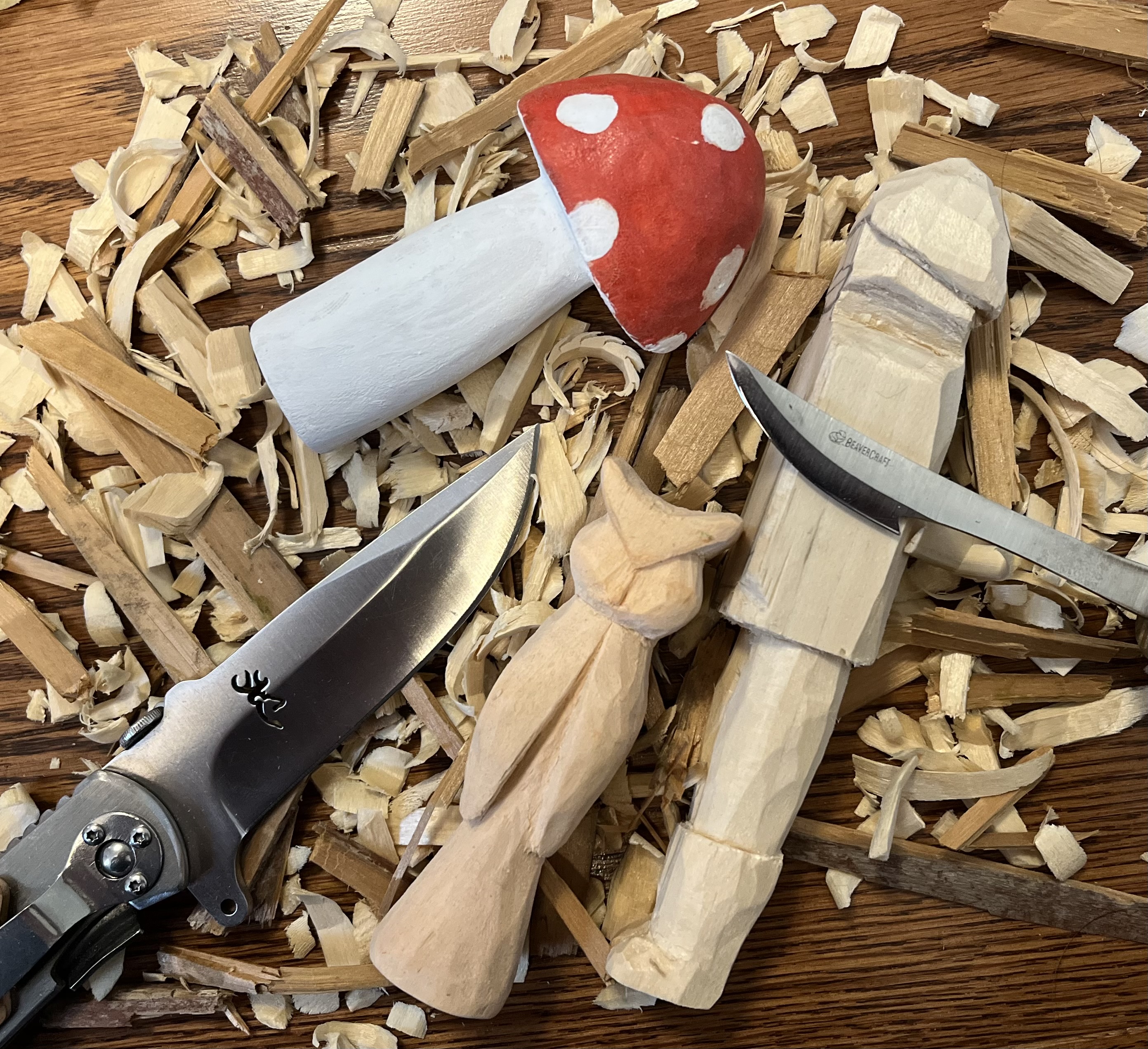 Wood carvings including a painted mushroom, cat, and robot with carving tools